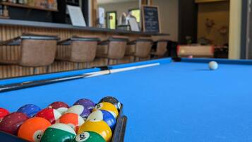 A pool table with balls, a bar area, and seating in a room.