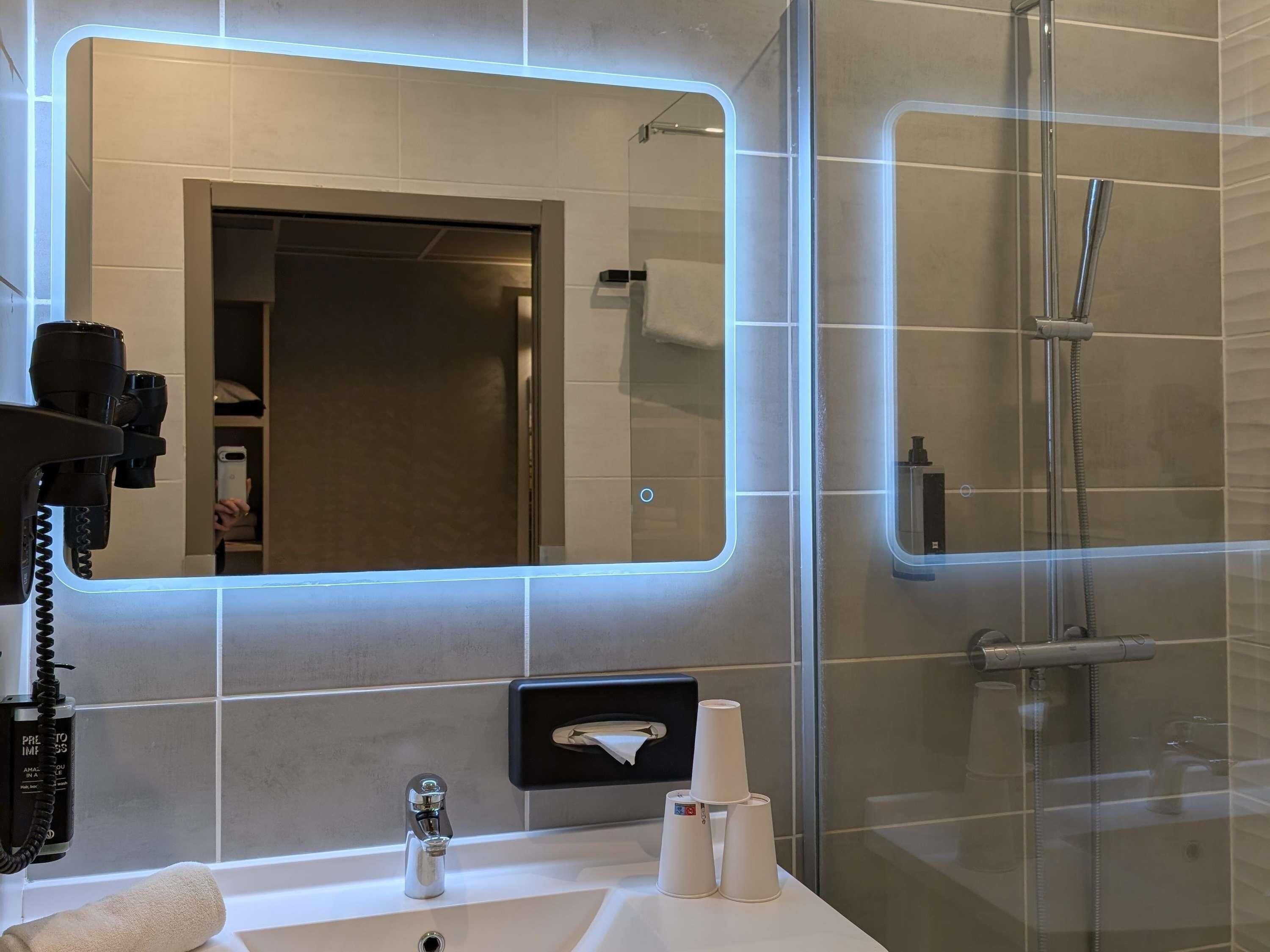 Un baño moderno con un espejo grande, un lavamanos, una toalla y una cabina de ducha de vidrio.