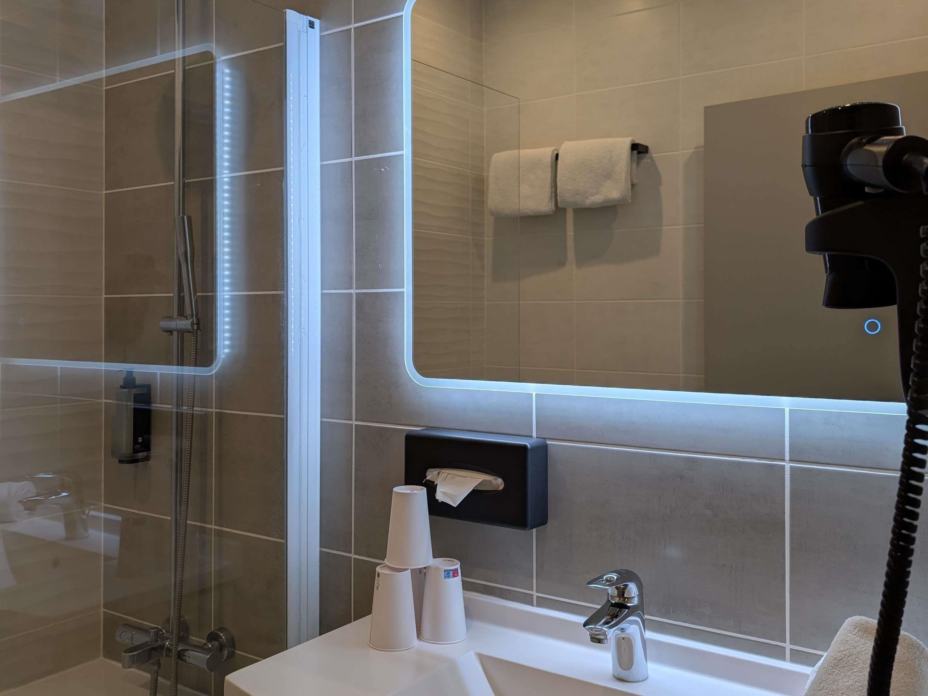 Une salle de bain moderne dotée d’une douche à parois de verre, d’un meuble-lavabo, d’un porte-serviettes et d’un sèche-cheveux fixé au mur.