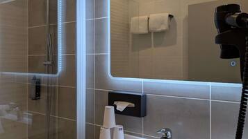 Une salle de bain moderne dotée d’une douche à parois de verre, d’un meuble-lavabo, d’un porte-serviettes et d’un sèche-cheveux fixé au mur.
