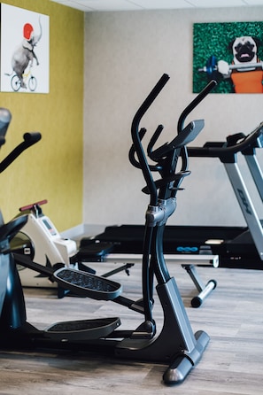 Une salle de sport équipée de vélos d’exercice et d’appareils elliptiques, dotée d’un plancher en bois et ornée d’œuvres d’art sur les murs.
