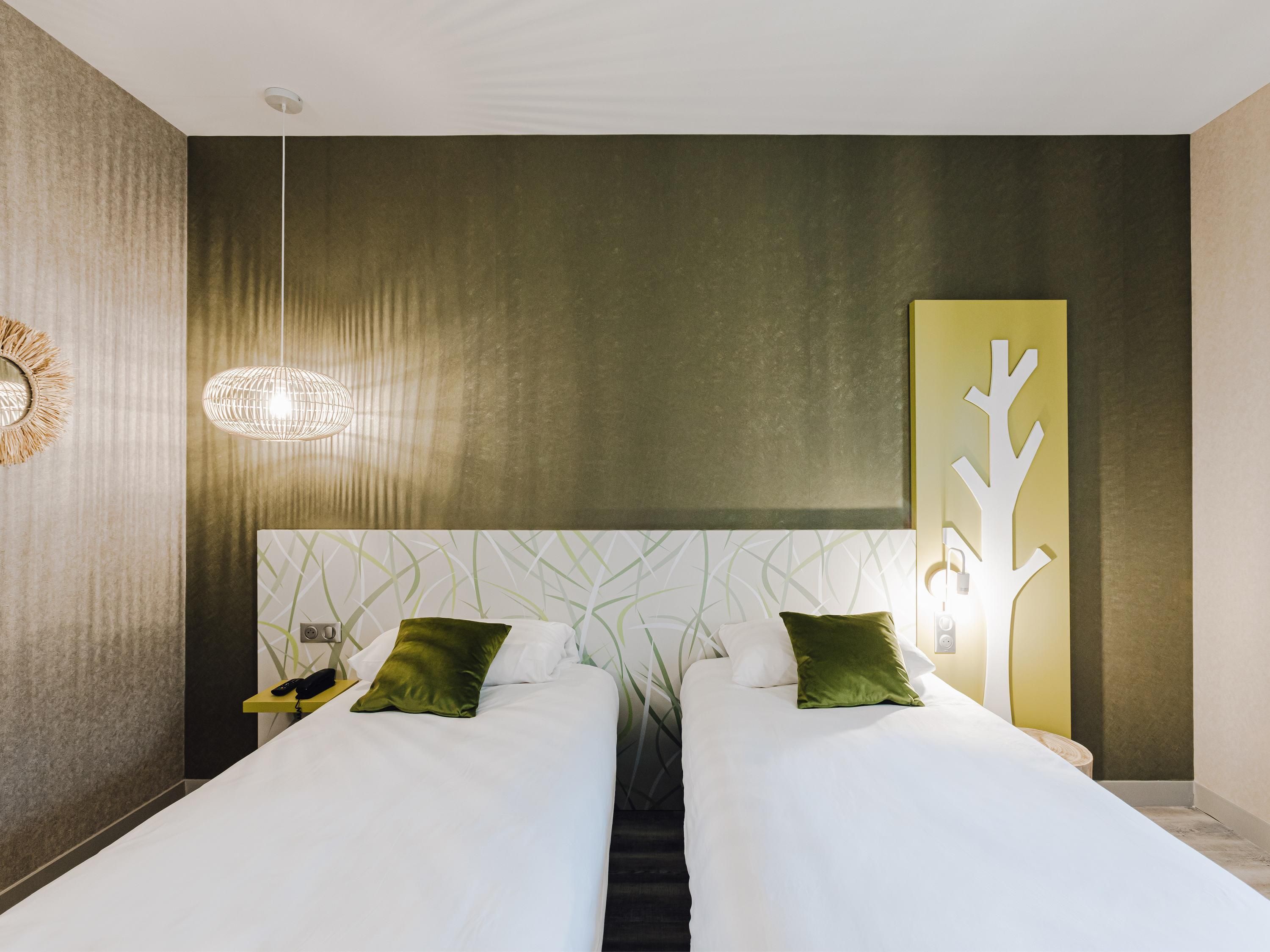 A double bed with white bedding and green pillows, a bedside table with a lamp, and a wall-mounted artwork.