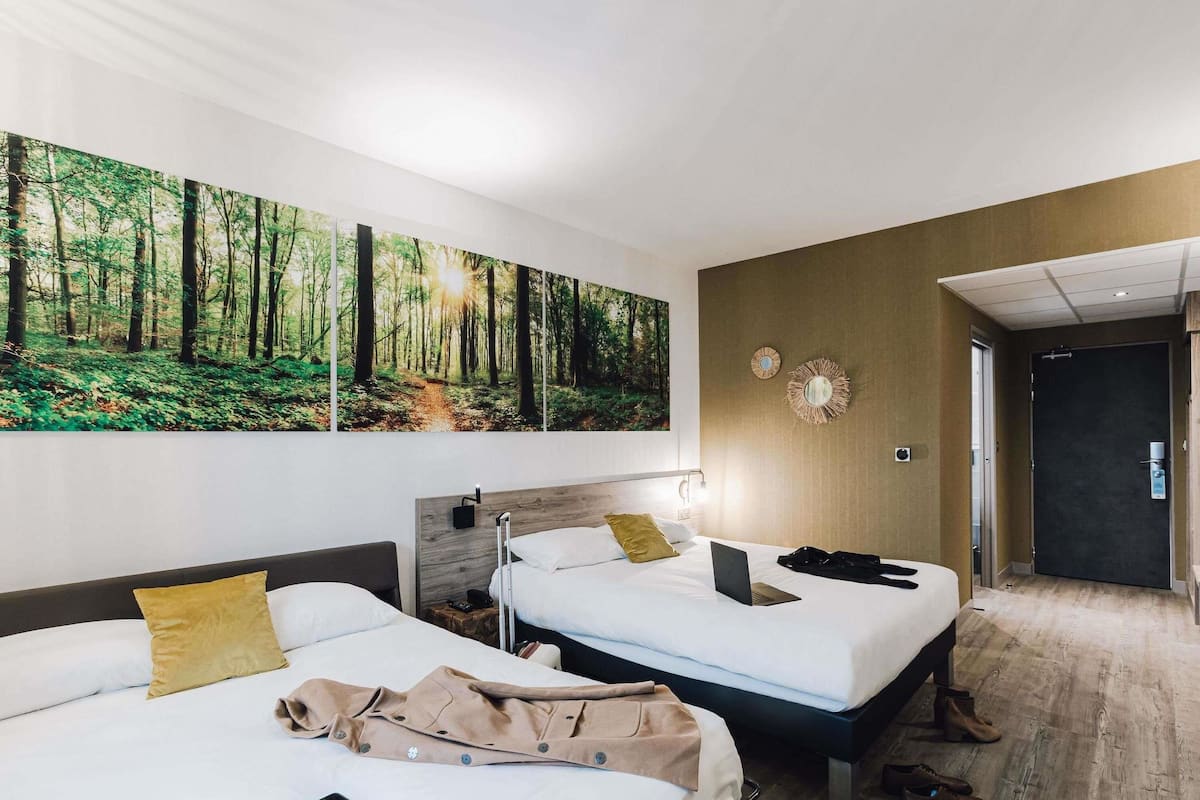 Une chambre dâhĂŽtel avec deux lits, une grande fresque murale sur le thĂšme de la forĂȘt, un miroir et une porte donnant sur le couloir.