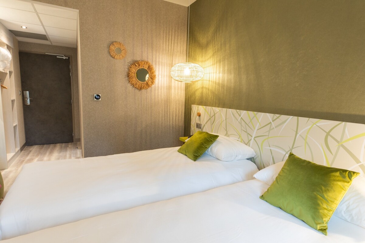 Une chambre d’hôtel comprenant un lit, une table de chevet, une lampe fixée au mur et une porte donnant accès à une salle de bain.