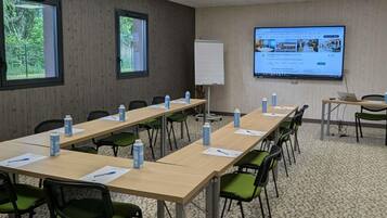 Ein Konferenzraum mit langen Tischen, grünen Stühlen, Wasserflaschen, einer Tafel und einer Projektionsleinwand, auf der eine Webseite angezeigt wird.