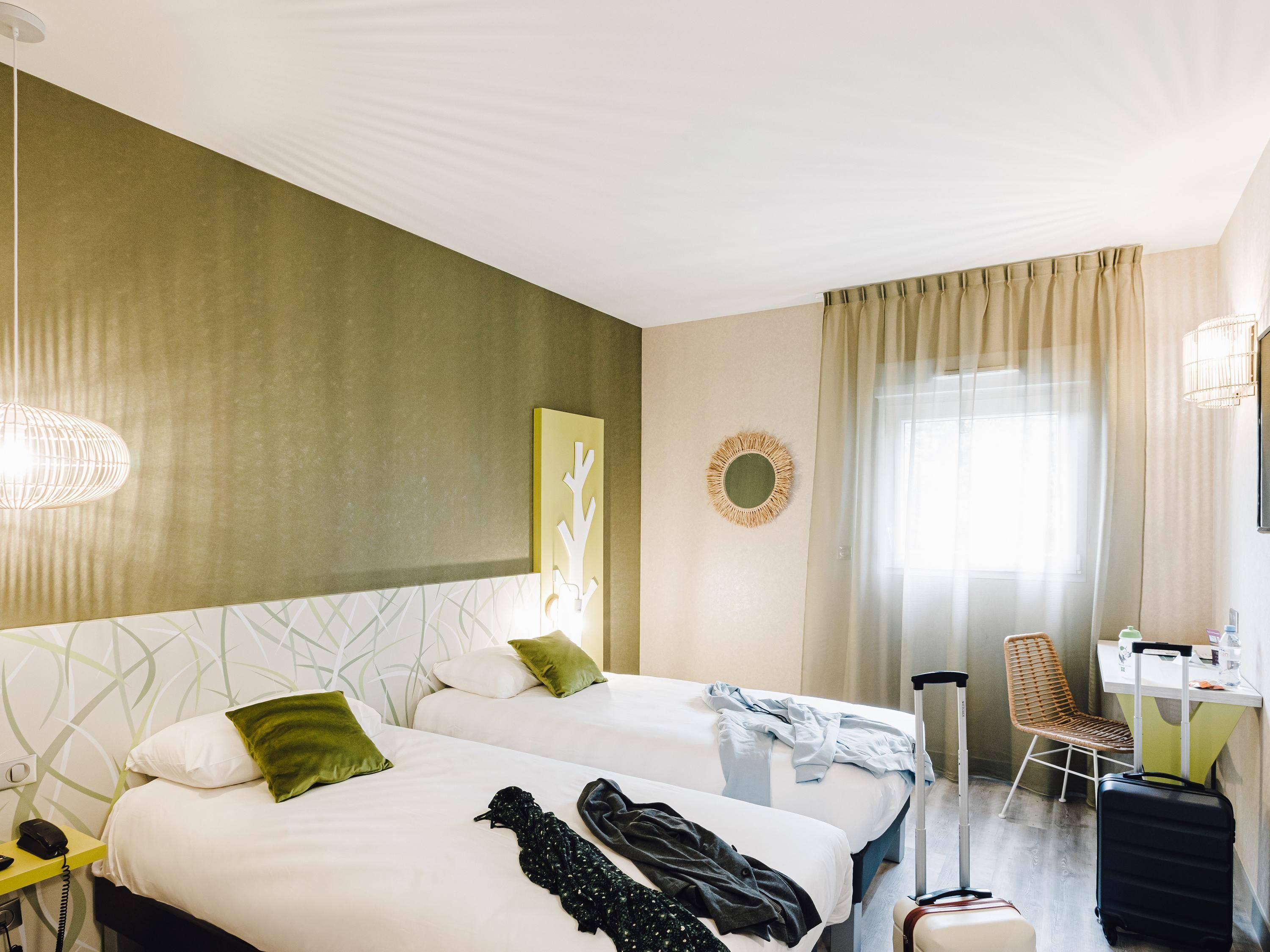 Een hotelkamer met twee bedden, een bureau, een stoel en een koffer.