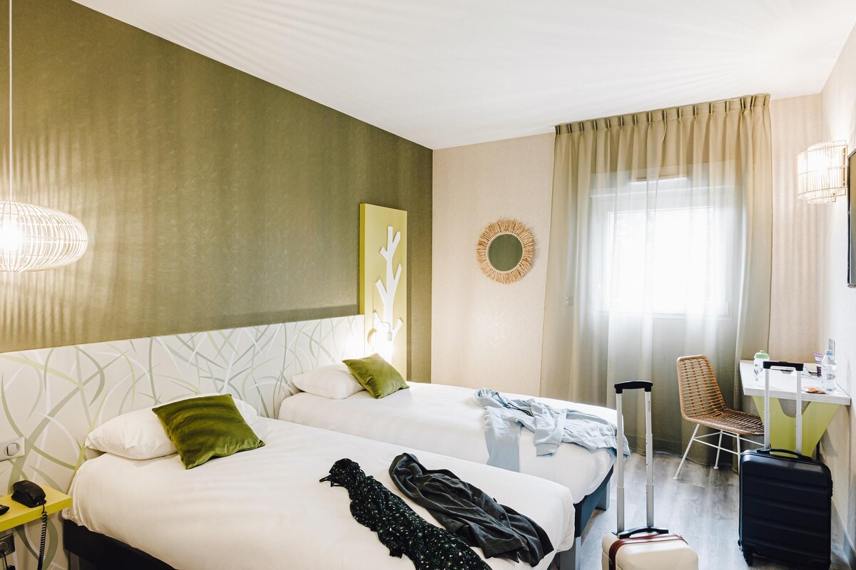 Une chambre d’hôtel avec deux lits, un bureau, une chaise et une valise.