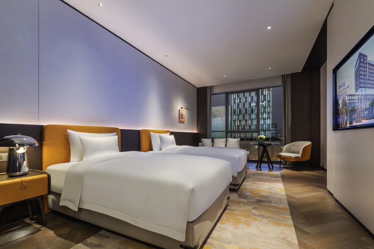 A modern hotel room with a large bed, bedside tables, a desk, and a chair.