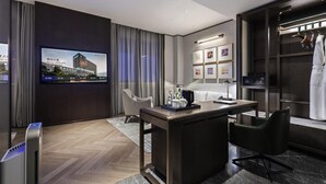 A modern hotel room with a flat-screen TV, a desk with a chair, a wardrobe, and a large window with curtains.