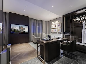 A modern hotel room with a flat-screen TV, a desk with a chair, a wardrobe, and a large window with curtains.