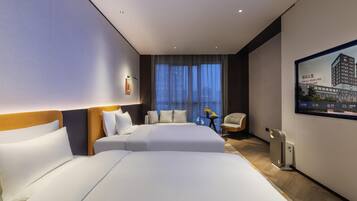 A modern hotel room with two beds, a seating area, a view of the city, and a large window.