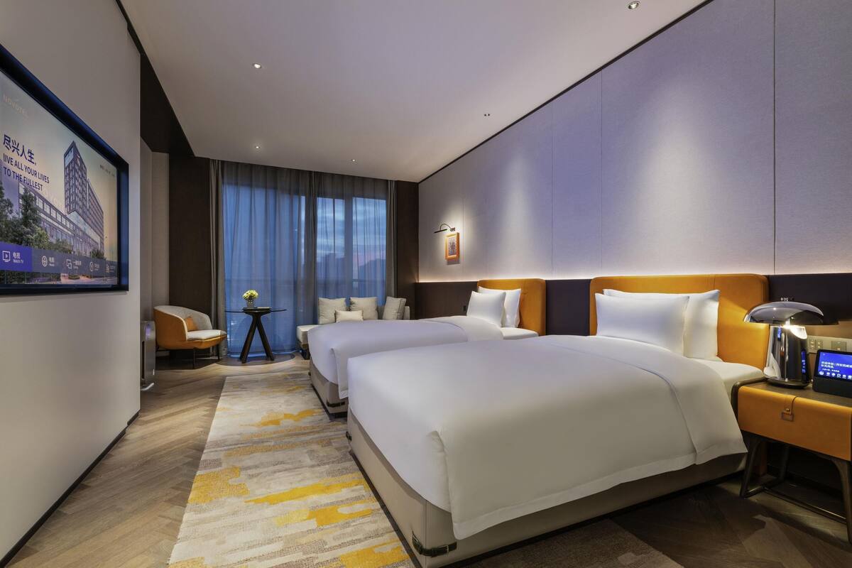 A hotel room with two beds, a desk, a chair, and a large window with curtains.