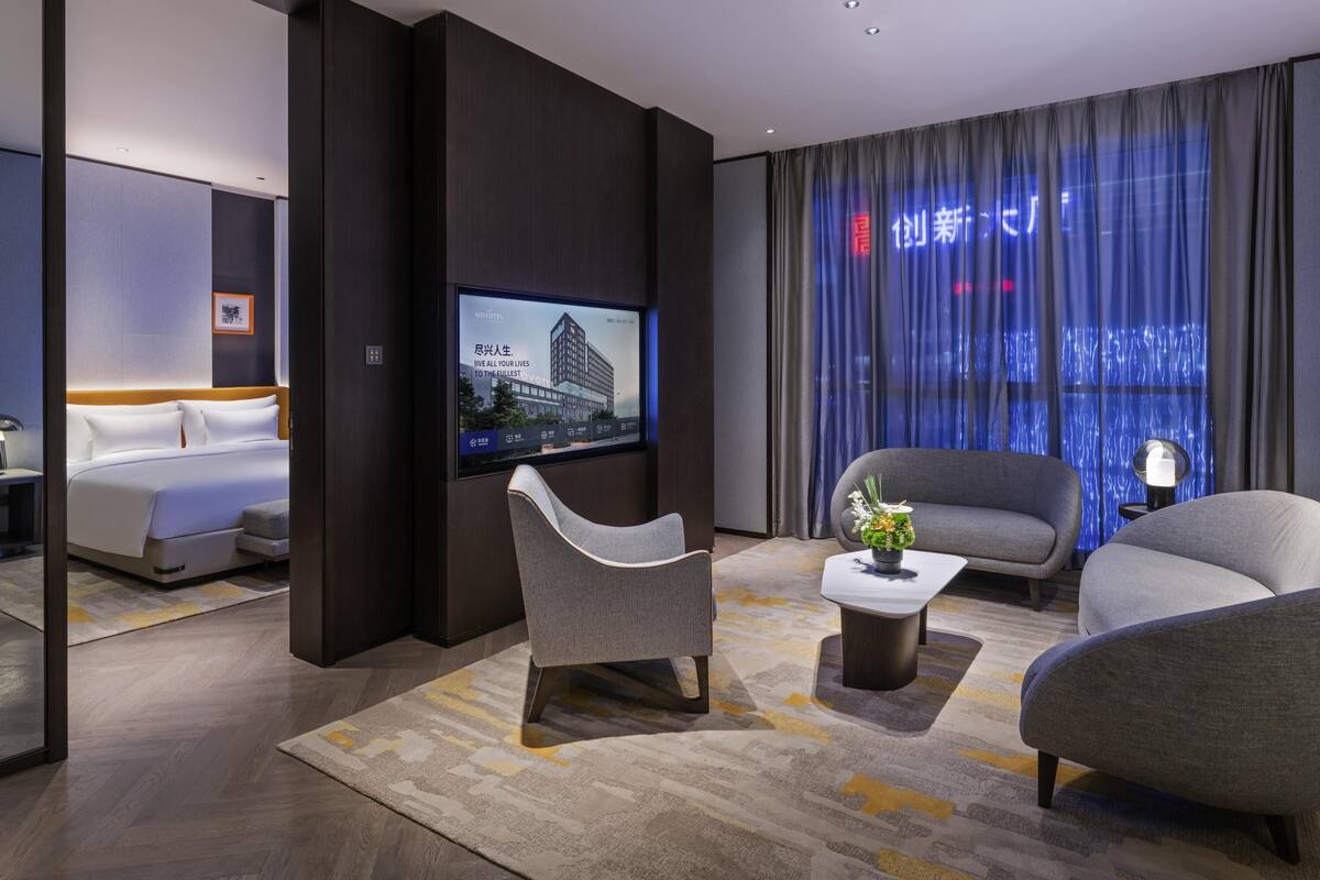 A modern hotel room with a bed, a TV mounted on the wall, a sofa, and a coffee table.