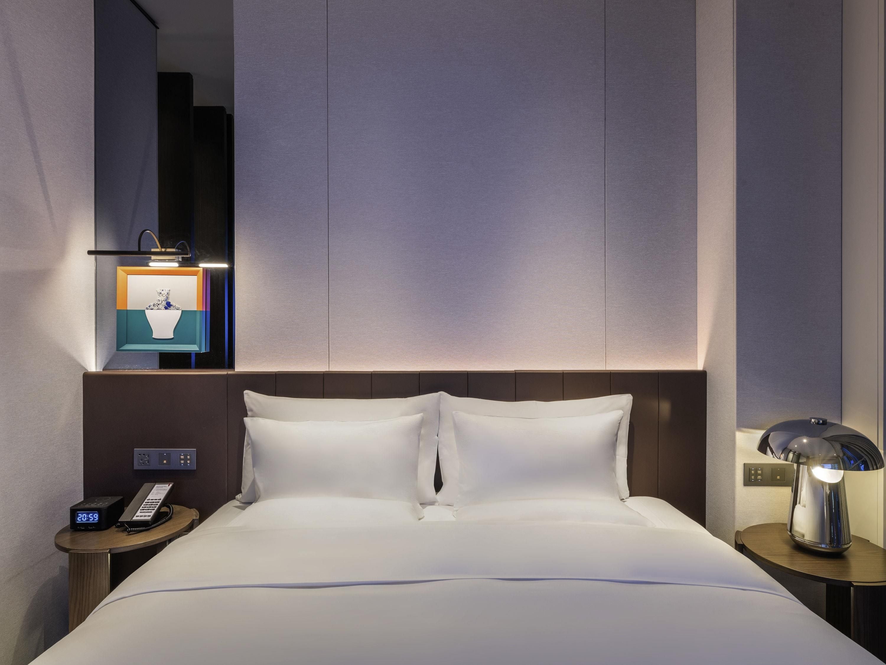 Une chambre d’hôtel comprenant un lit, des tables de chevet, une petite table, une lampe, un téléphone et un luminaire fixé au mur.