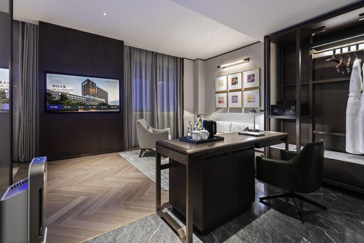 A modern hotel room with a flat-screen TV, a desk with a chair, a wardrobe, and a bed.