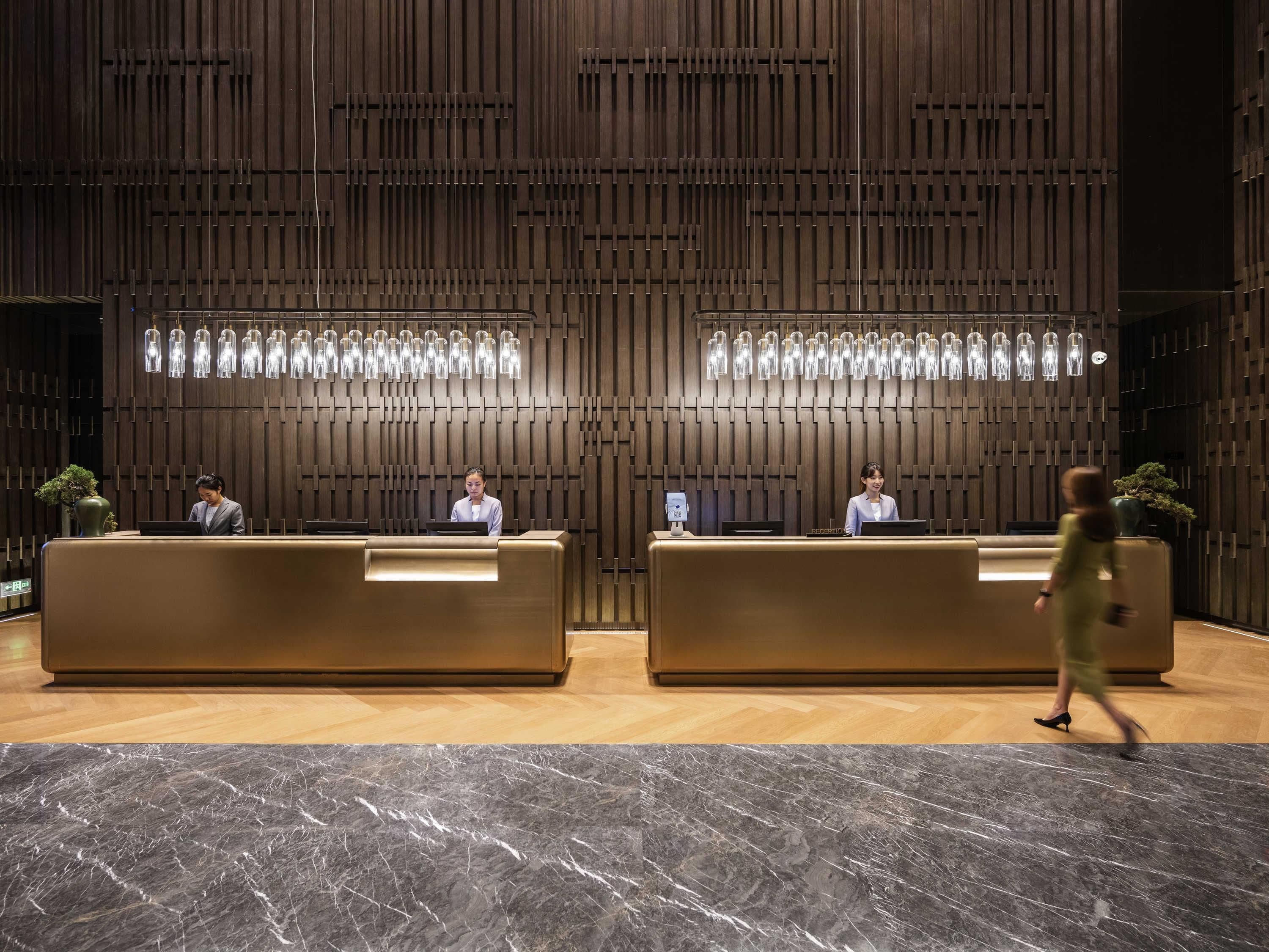 Un área de recepción con dos mostradores, una pared de madera con listones verticales y un piso de mármol.