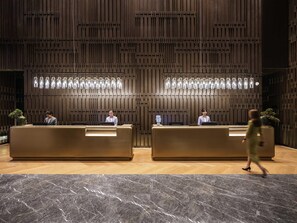 Un área de recepción con dos mostradores, una pared de madera con listones verticales y un piso de mármol.