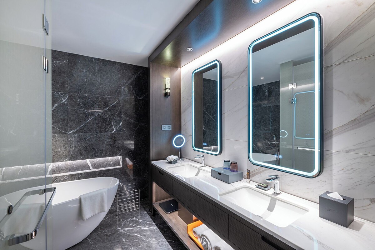 A modern bathroom with a bathtub, two sinks, and large mirrors with illuminated frames.