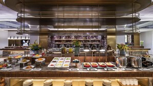 Ein Buffet mit verschiedenen Speisenstationen, ein Koch bereitet Speisen zu und ein Marmorbelag ist im Hintergrund zu sehen.