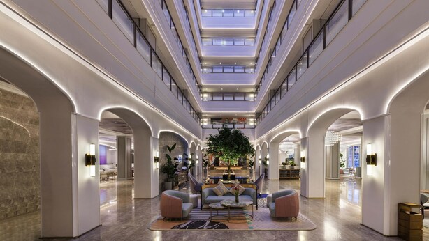 Eine großzügige Lobby mit hoher Decke, Oberlichtern und einer zentralen Sitzecke mit Sofas und Couchtisch.