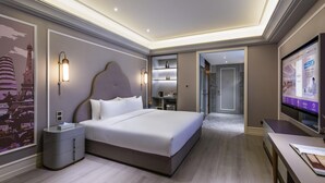 Ein modernes Hotelzimmer mit einem großen Bett, Nachttischen, einem Fernseher und einem durch eine offene Tür einsehbarer Badezimmer.