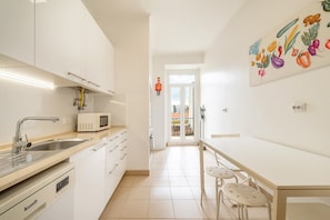 A modern kitchen with white cabinetry, a microwave, a sink, and a dining area with a table and chairs.