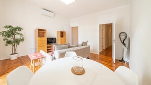 A modern living room with a dining table, sofa, TV stand, and a potted plant. - GuestReady - Tower- 3 Bedroom Apt in Saldanha (Lisboa)