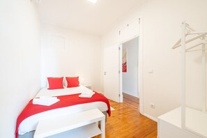 A bedroom with a bed, a bedside table, a wardrobe, and a door leading to another room.