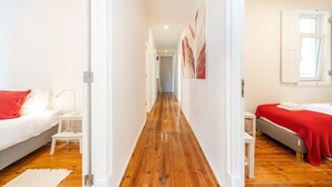 A hotel room with a wooden floor, white walls, a bed with a red blanket, a bedside table, and a window. - GuestReady - Tower- 3 Bedroom Apt in Saldanha (Lisboa)