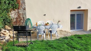 An outdoor patio with a table and chairs, a grill, and a door leading to a covered area. - Maison au Calme à Proximité des Plages (Querrien)