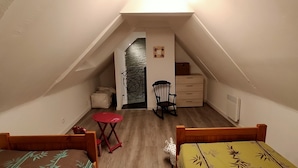 A small, narrow attic bedroom with two wooden beds, a red table, a chair, a dresser, and a radiator. - Maison au Calme à Proximité des Plages (Querrien)