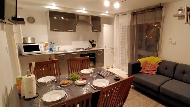 A compact living space with a dining area, kitchenette, and a sofa. - Maison au Calme à Proximité des Plages (Querrien)