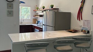 A modern kitchen with a marble countertop, stainless steel appliances, and bar stools. - Jazmin Del Sol - Just Steps Away to the Beautiful Potrero Beach (Potrero)