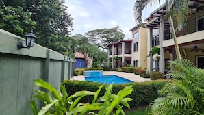 A residential building with a swimming pool surrounded by lush greenery and palm trees. - Jazmin Del Sol - Just Steps Away to the Beautiful Potrero Beach (Potrero)