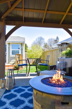 An outdoor patio with a stone fire pit, seating area, and a view of a house in the background. - Vivid colorful craftsman with patio and fire pit (Seattle)