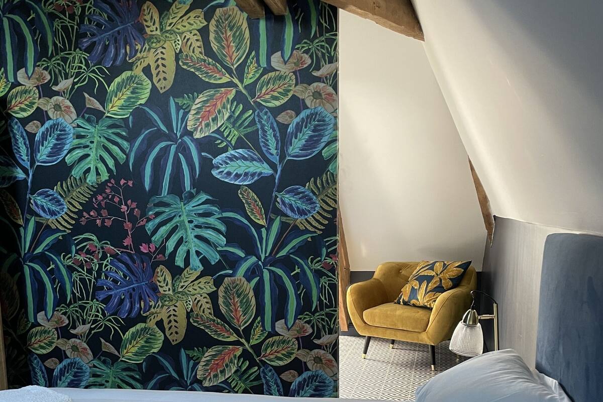 Een slaapkamer met een bed, een gele fauteuil en een levendig tropisch behang.