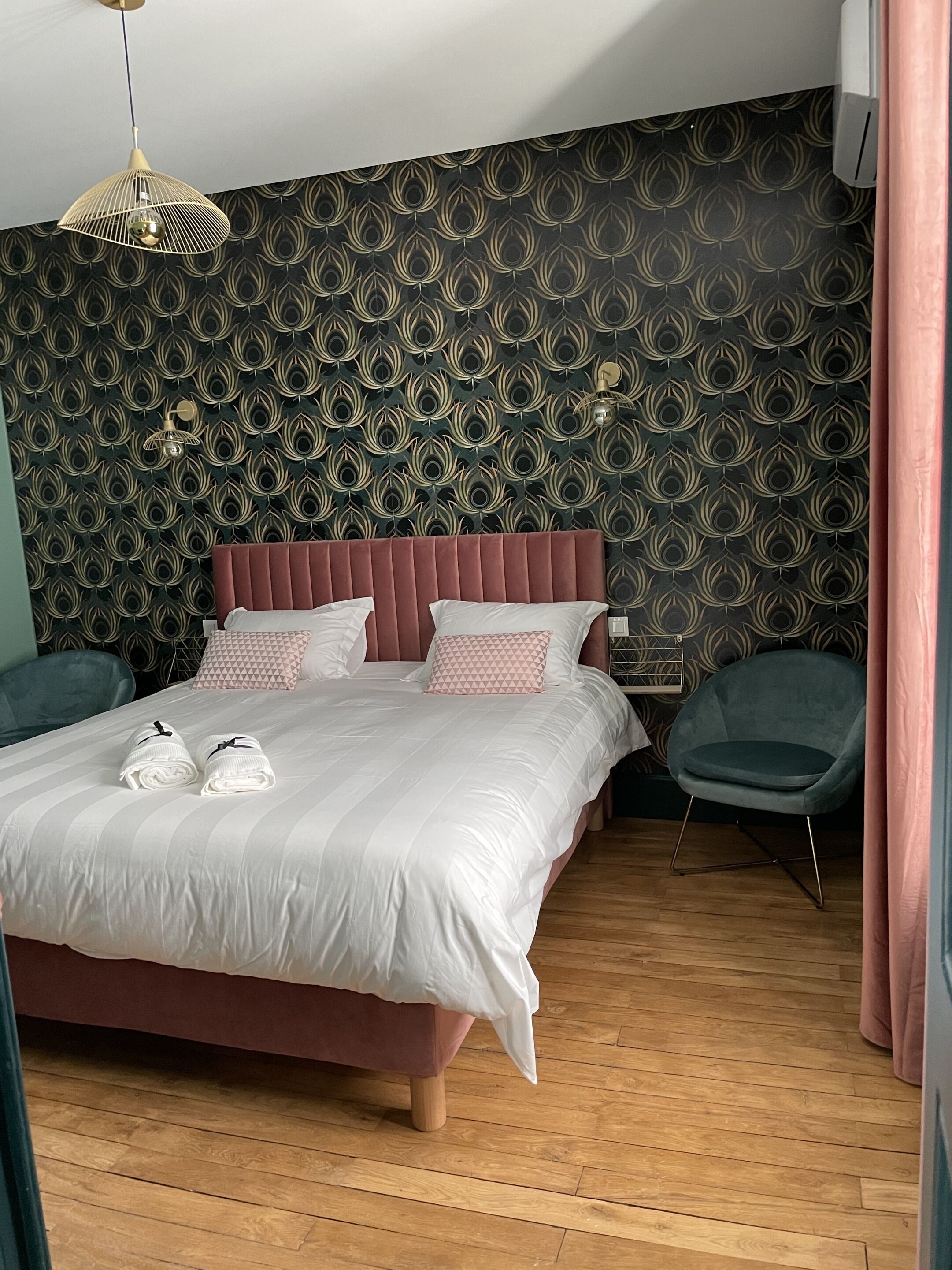 Un dormitorio moderno con papel tapiz estampado, una cama grande con ropa de cama blanca, dos mesitas de noche y una lámpara colgante.