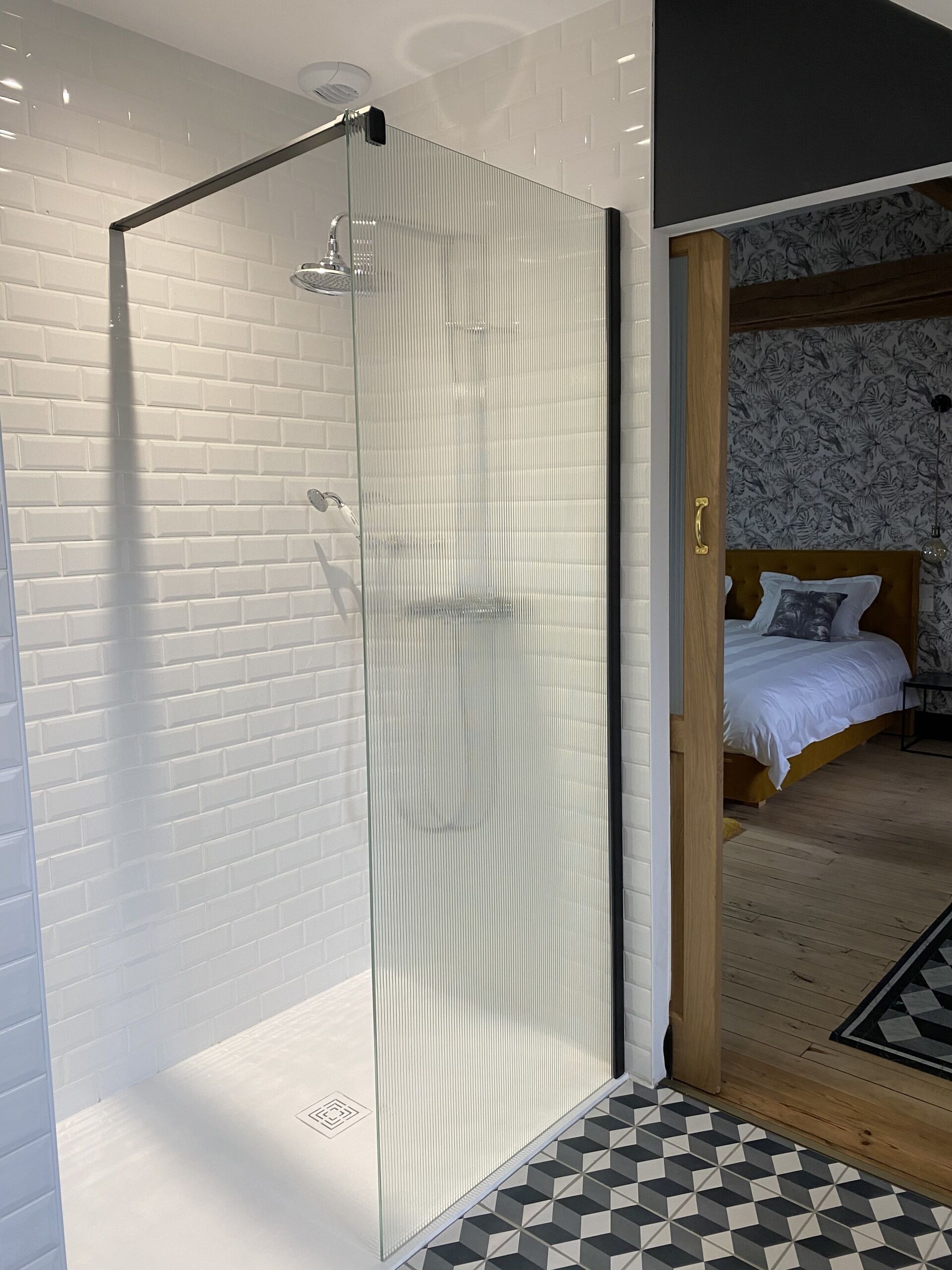 Un baño moderno con cabina de ducha de vidrio, azulejos blancos tipo metro y suelo con diseño geométrico.