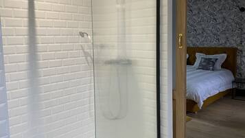 Un baño moderno con cabina de ducha de vidrio, azulejos blancos tipo metro y suelo con diseño geométrico.