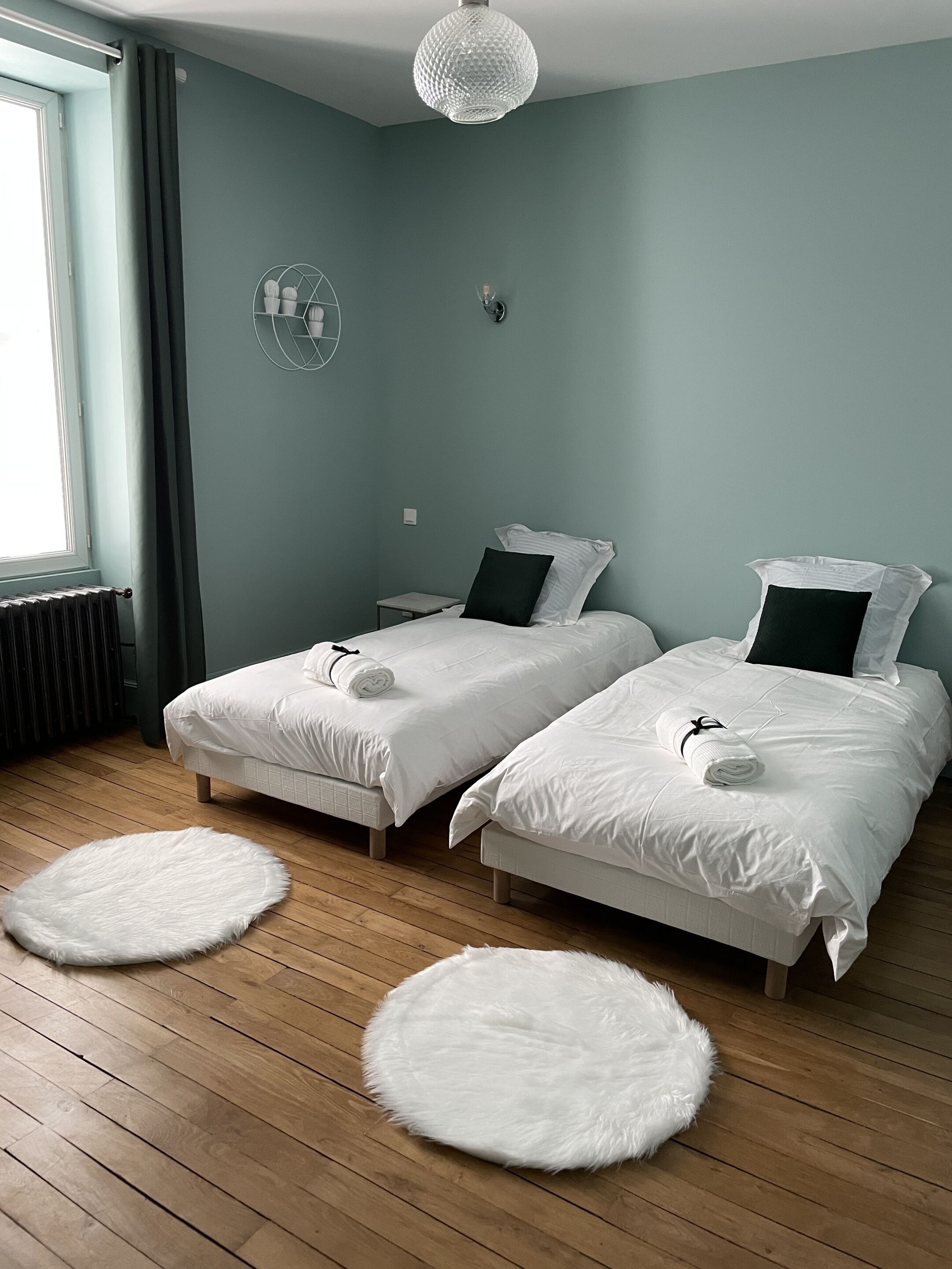 Une chambre avec deux lits, un tapis rond blanc, un radiateur et un luminaire suspendu.