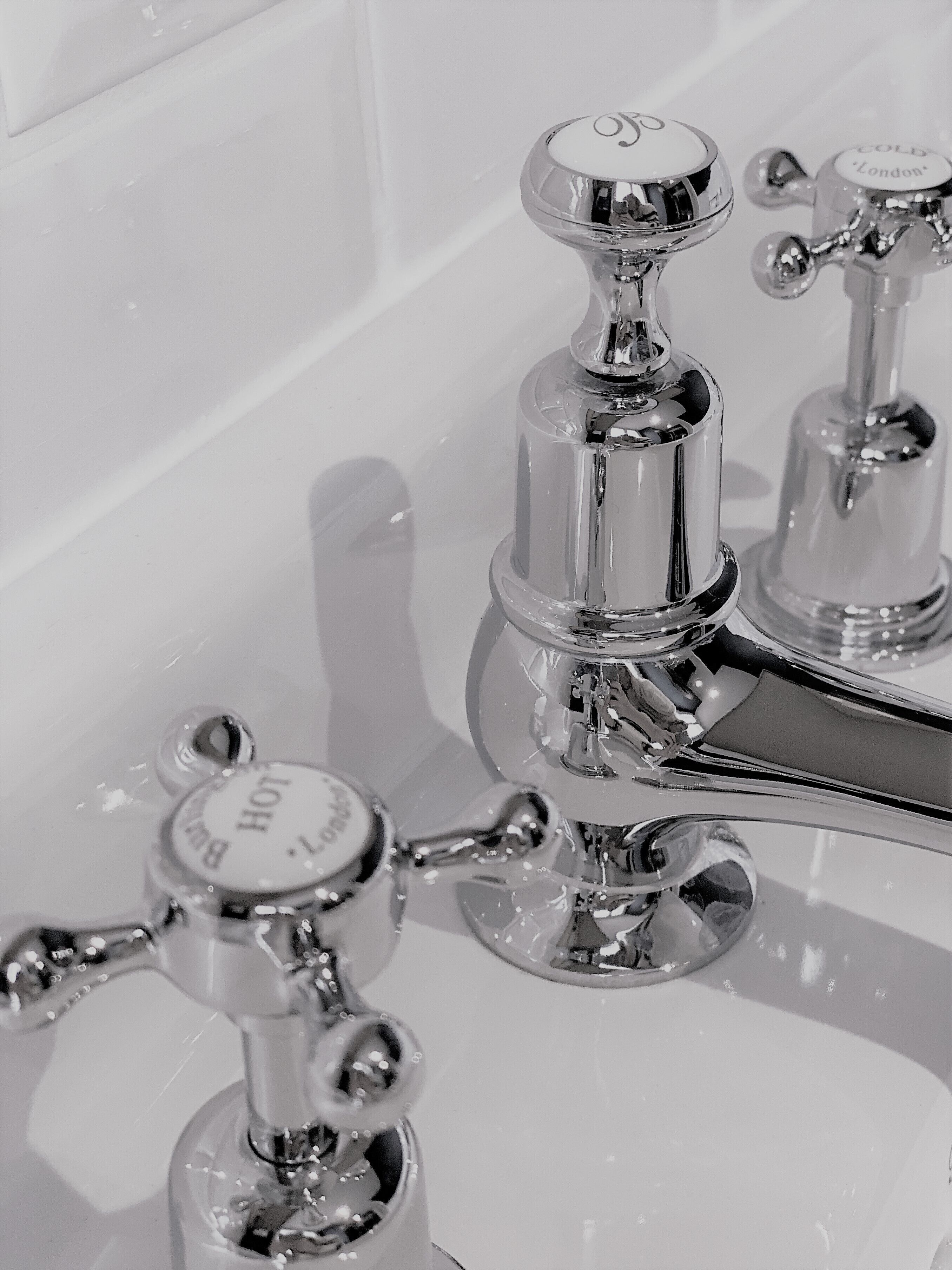 A bathroom with chrome fixtures, including a sink with a faucet labeled 'HOT' and 'COLD', and a mirror.