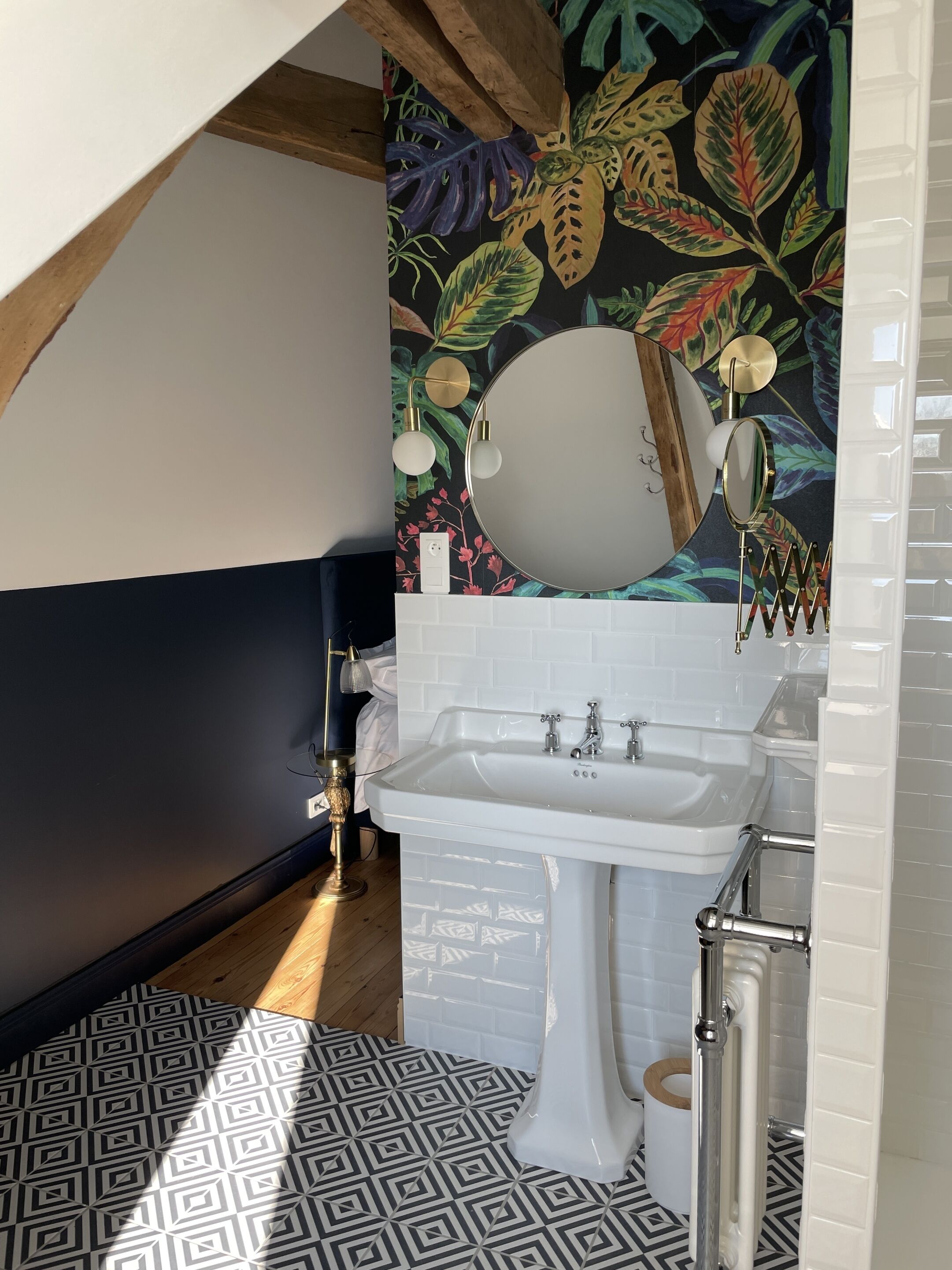 A bathroom with a white sink, a mirror, and a decorative wall with a tropical leaf pattern.
