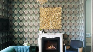 Un salon avec une cheminée, un papier peint à motifs, un canapé bleu, une petite table et un fauteuil bleu.