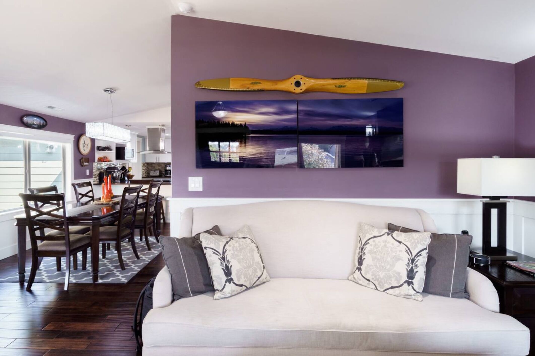 A living room with a sofa, a dining table, and chairs. There is a painting of a boat on the wall.
