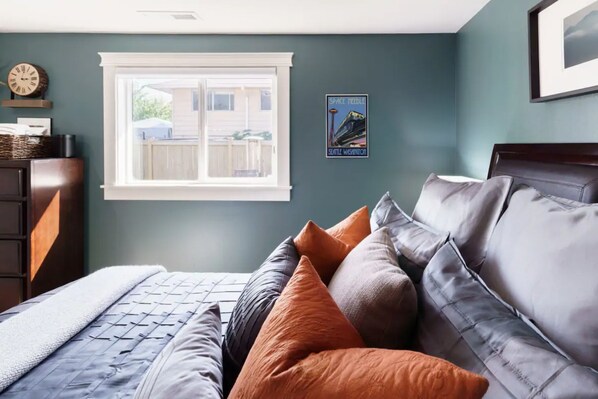 Een slaapkamer met een bed, kussens, een dressoir, een raam en een poster aan de muur.
