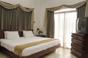 A hotel room with a large bed, a television on a wooden dresser, and curtains on the windows.