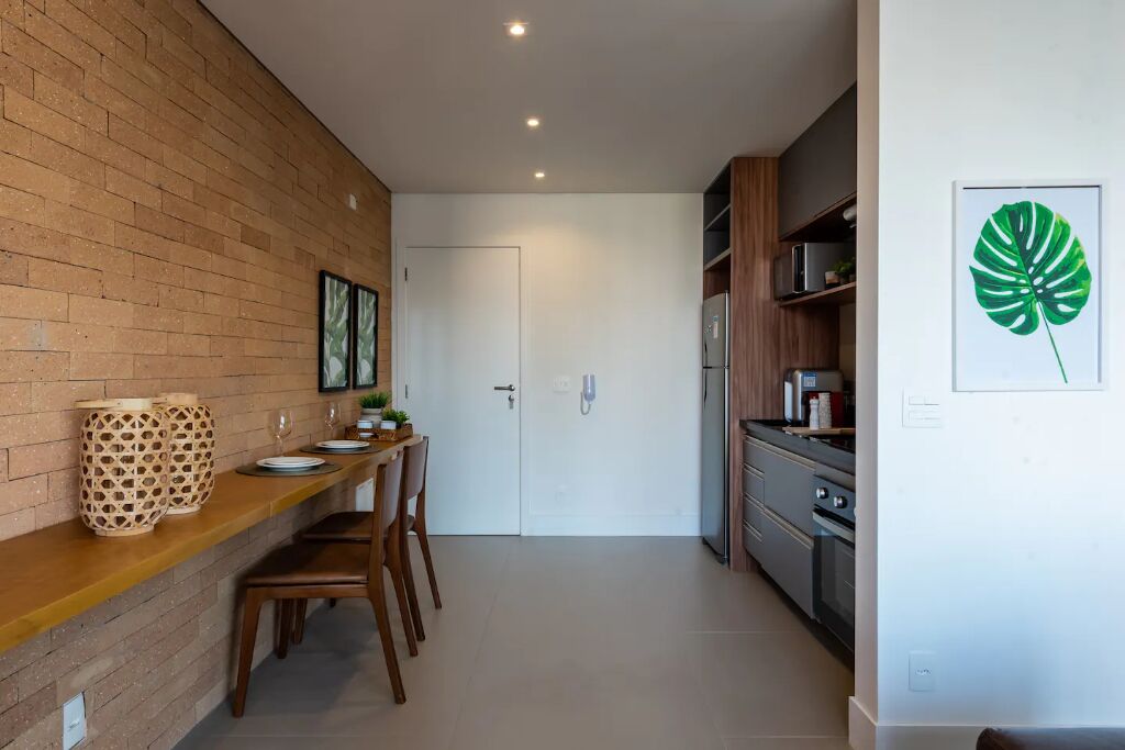 A modern kitchen with a brick wall, wooden countertop, and a dining area with chairs.