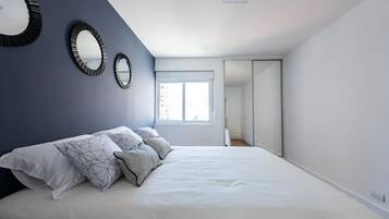 A bedroom with a bed, two wall mirrors, a window, and a door leading to another room.