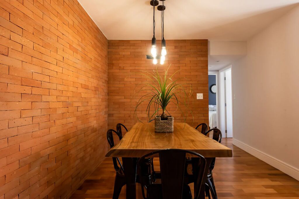 A dining area with a wooden table and chairs, a brick wall, and a hanging light fixture.