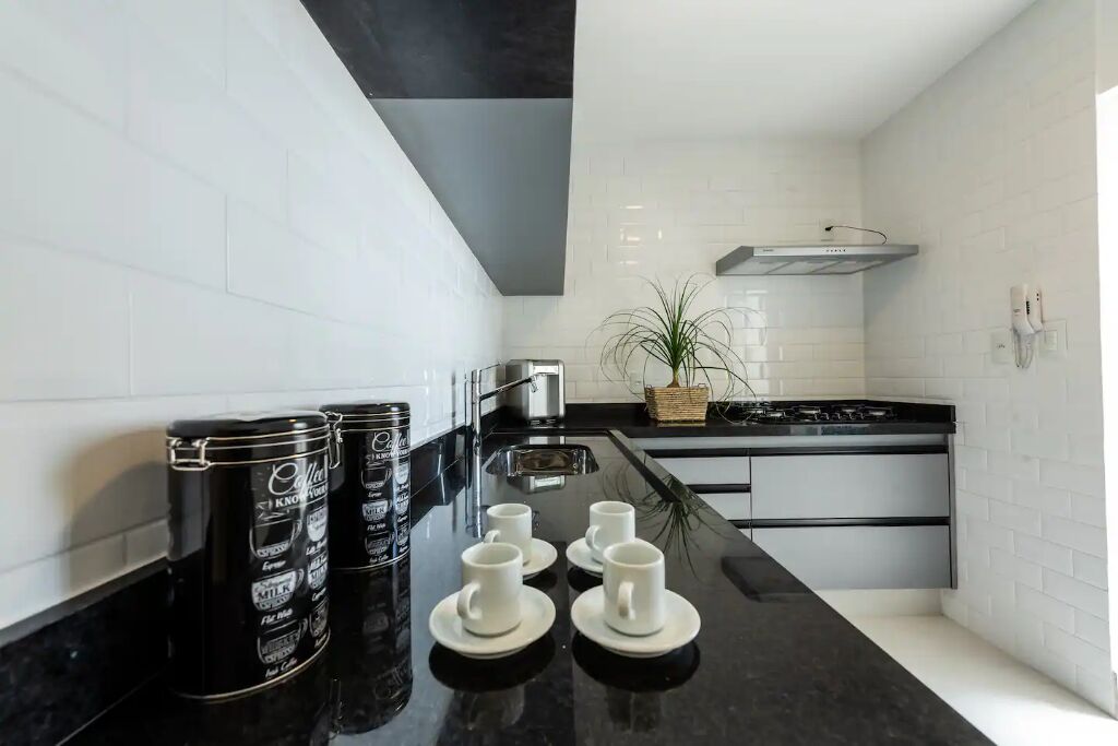 A modern kitchen with white subway tiles, black countertops, and stainless steel appliances. There are three coffee cans, four white cups, and a potted plant on the counter.
